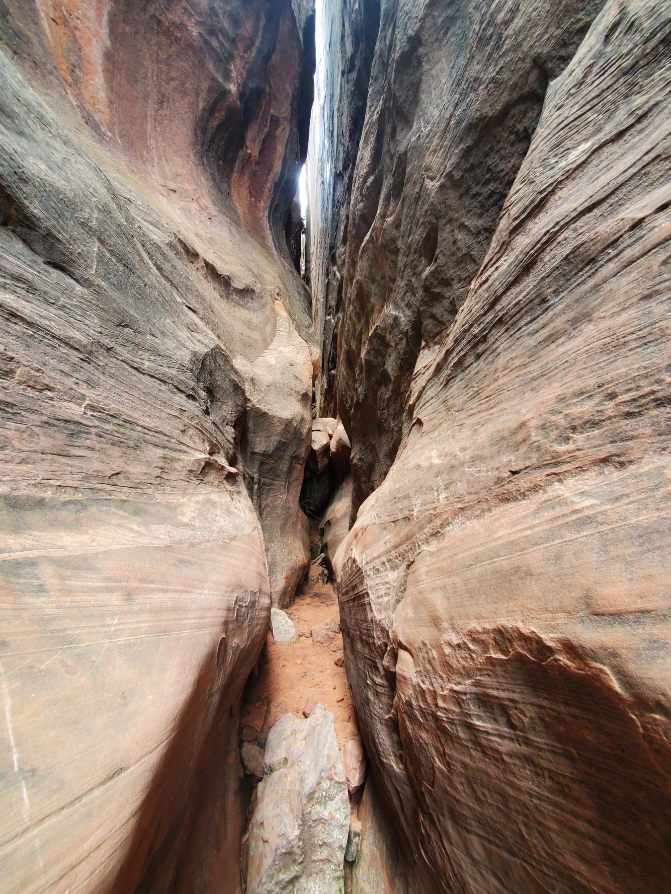 A person moving carefully through a narrow water-carved sandstone passage